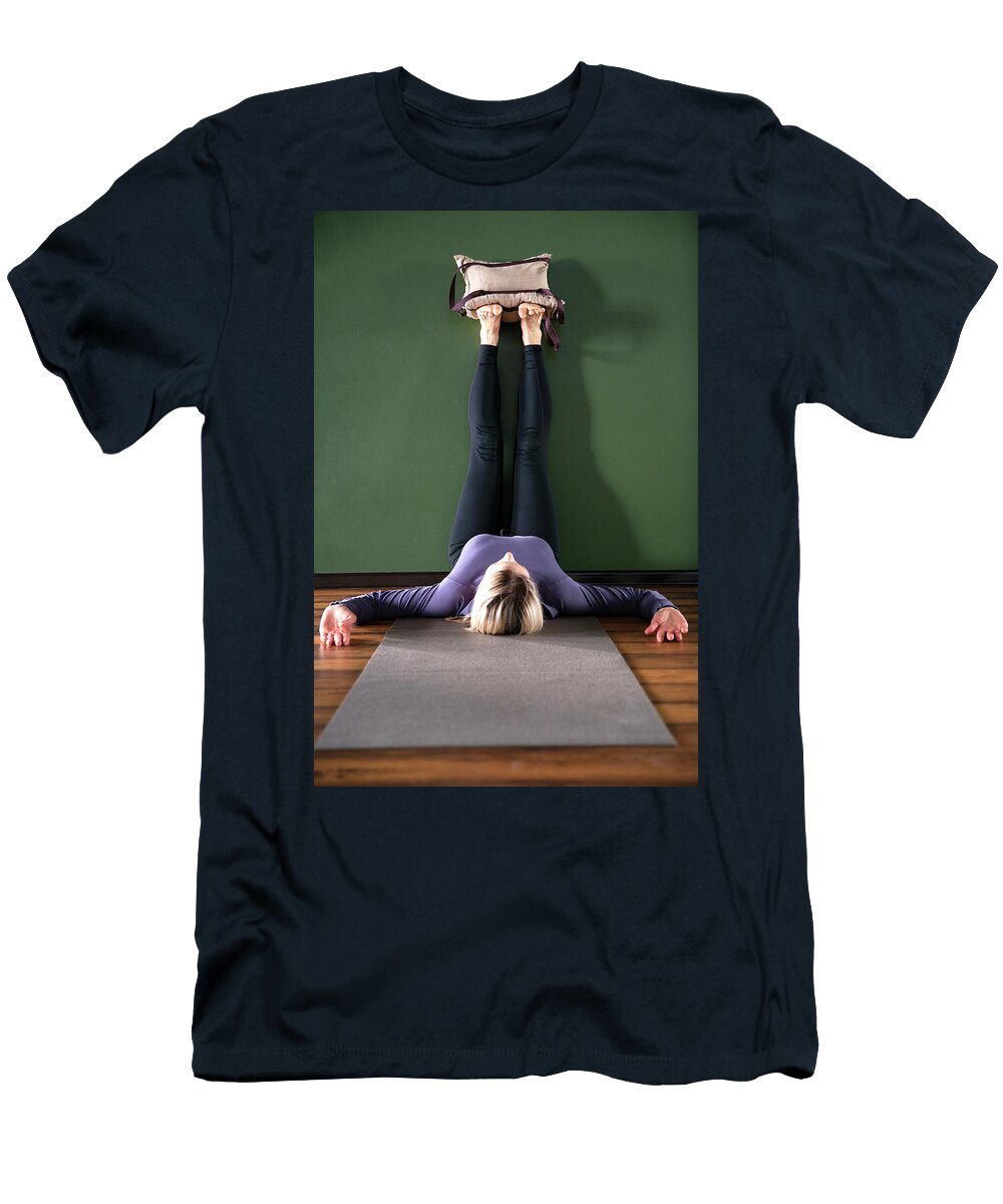 Young Woman in Yoga Relaxing Pose with Legs Up Against Wall with Heavy Sand Bags Maria Kray T-Shirt